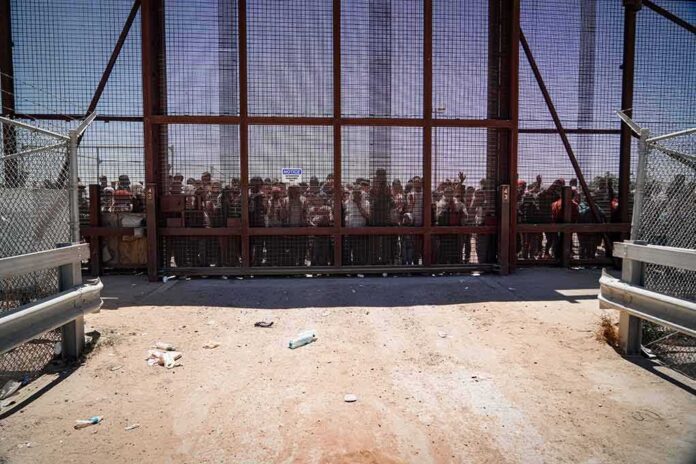 Crowd stands behind tall metal fence at border crossing