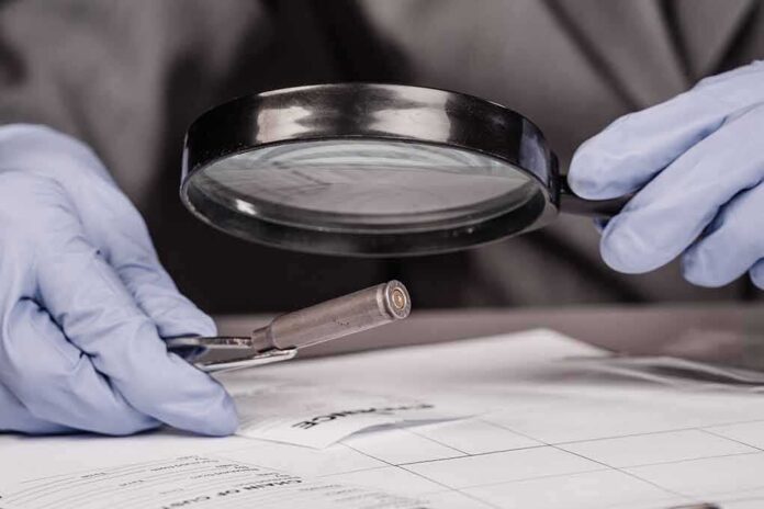 Gloved hands examine bullet casing with magnifying glass