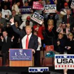 Donald Trump addresses a rally crowd at a podium, raising his fist