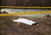 covered body at riverside crime scene with evidence markers