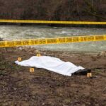 covered body at riverside crime scene with evidence markers