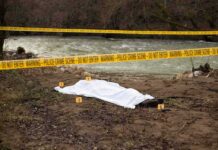 covered body at riverside crime scene with evidence markers